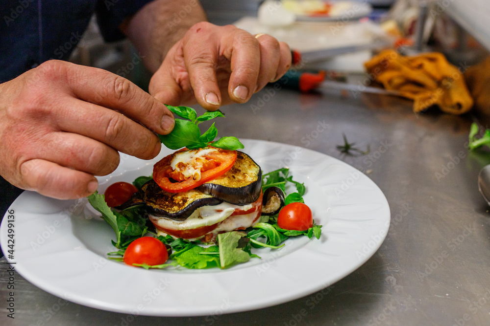Chef mentre guarnisce una millefoglie di melanzane, mozzarella e pomodoro con del basilico fresco Chef mentre guarnisce una millefoglie di melanzane, mozzarella e pomodoro con del basilico fresco