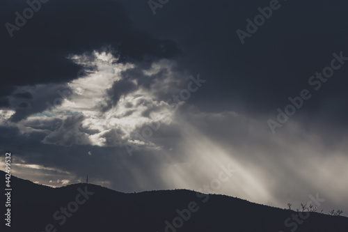 thick stormy clouds over the mountains with intense sun rays peaking through and contrasty light