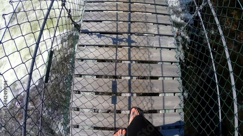 Woman walking on a suspension bridge over a rippling raging river. Point of view, looking down. Mårdseleforesen, North of Sweden. Summertime.  photo