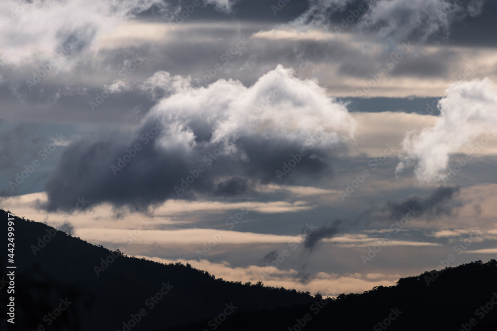 thick stormy clouds over the mountains with intense sunlight peaking through and contrasty tones thick stormy clouds over the mountains with intense sunlight peaking through and contrasty tones
