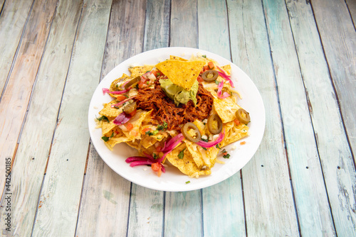 Mexican corn nachos with avocado guacamole, cochinita pibil meat and sliced jalapenos on white plate