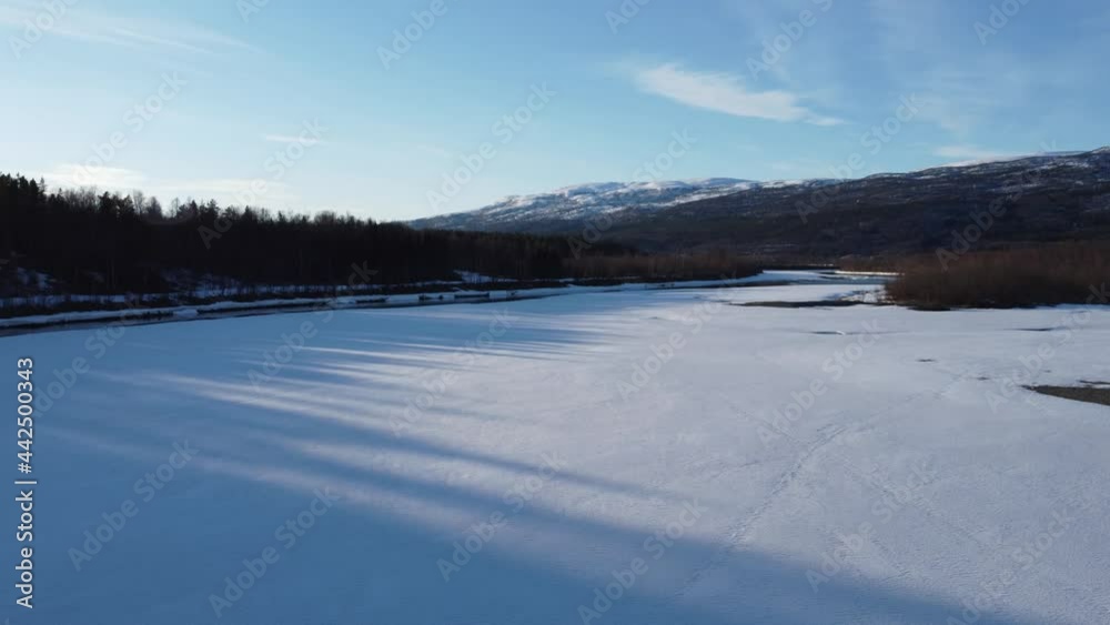 flying over snow patch covered river shore with clean cold melting water running through the river and mighty forest and snowy peak mountain in the backdrop, aerial video flying over snow patch covered river shore with clean cold melting water running through the river and mighty forest and snowy peak mountain in the backdrop, aerial video