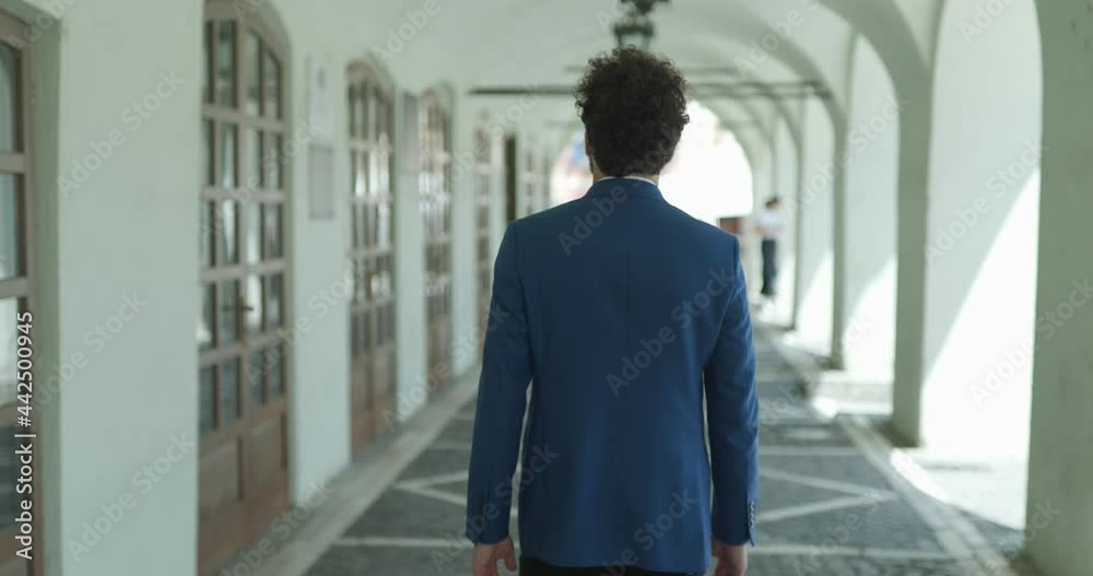back view of smart casual guy with curly hair walking outside, looking to side and admiring city while posing back view of smart casual guy with curly hair walking outside, looking to side and admiring city while posing
