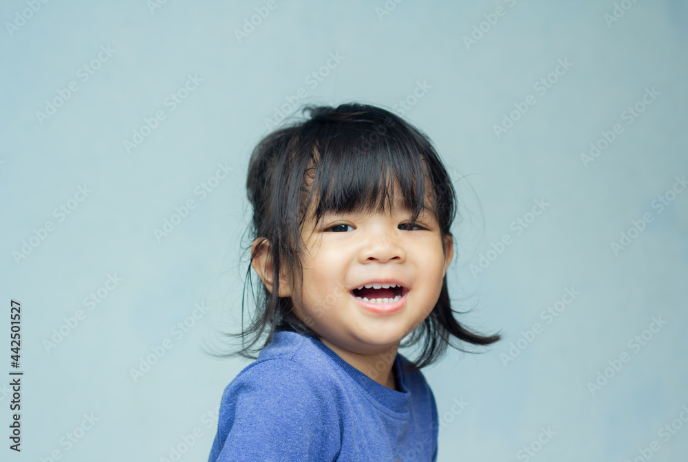 A headshot portrait of a cheerful baby Asian woman, a cute toddler little girl with adorable bangs hair, a child wearing a blue sweater smiling and looking to the camera.