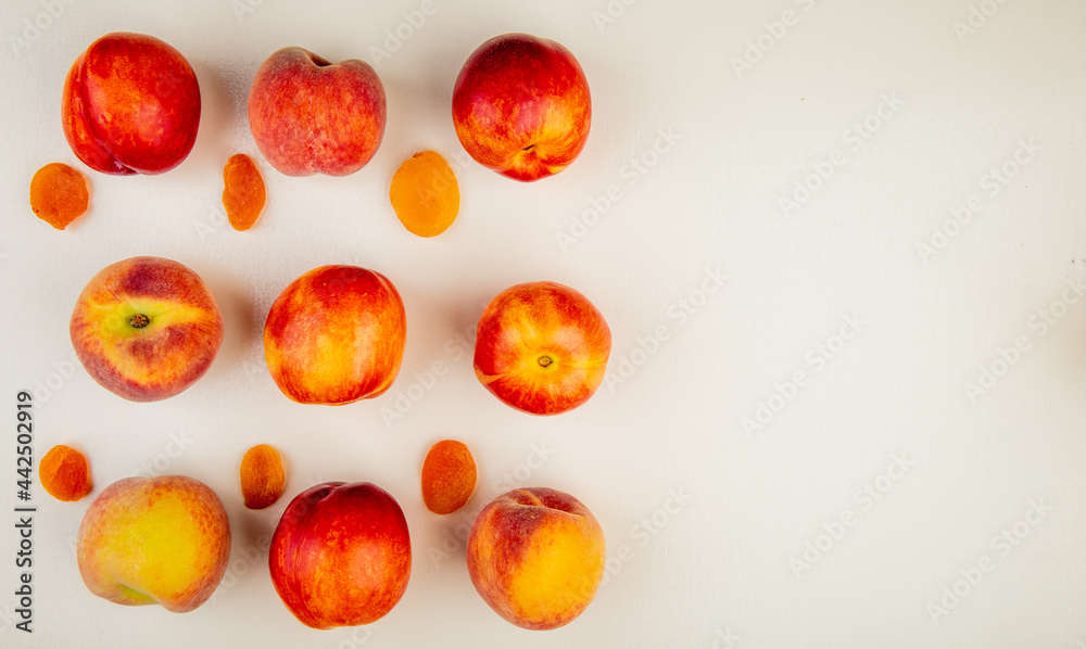 Fototapeta premium top view of fresh ripe nectarines and peaches with dried apricots on white background with copy space
