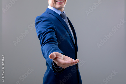 Smiling caucasian businessman reaching his hand, isolated on grey background photo