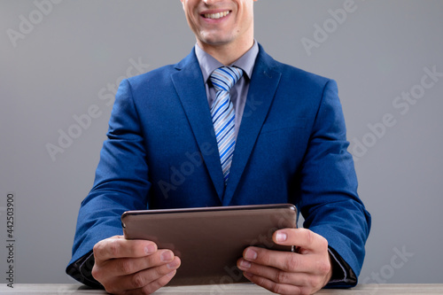 Smiling caucasian businessman using tablet, isolated on grey background