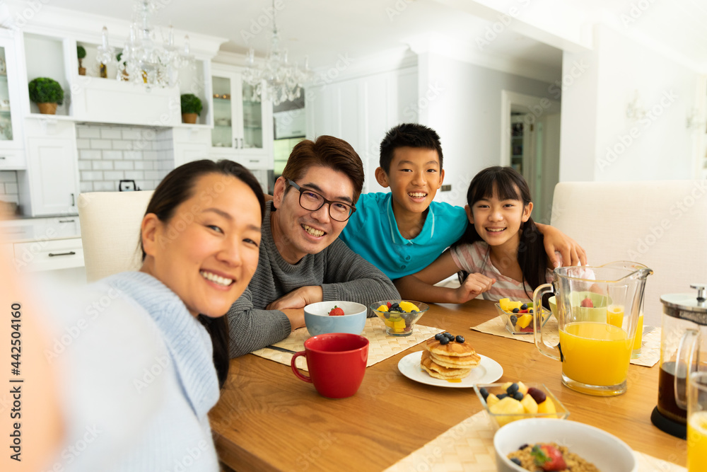 Asian couple with son and daughter sitting at table eating together at home