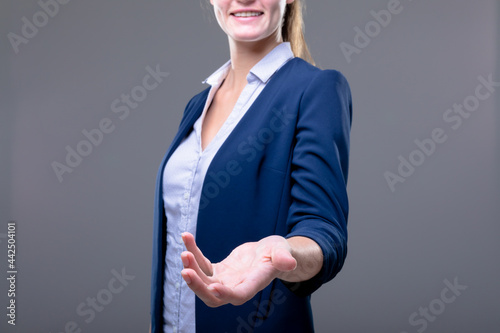 Smiling caucasian businesswoman reaching with her hand, isolated on grey background