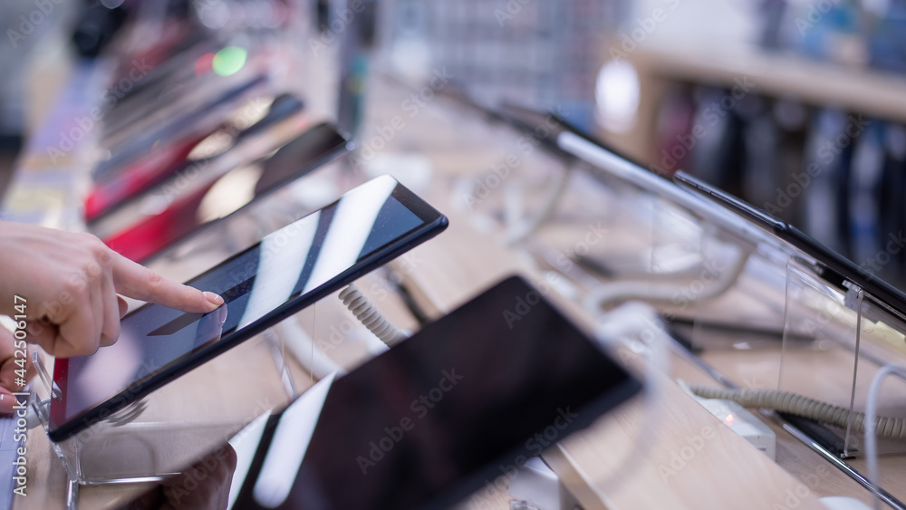 Obraz premium Faceless caucasian woman chooses a smartphone in an electronics store. Close-up of a female hand with a phone tester