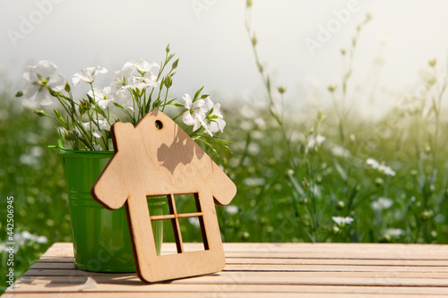 on a wooden table a small decorative bucket with a bouquet of white flowers and a small house, concept