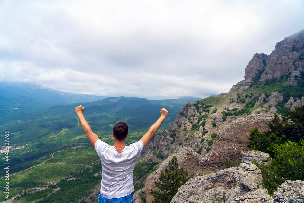 Panoramic view of tourist on mountains hill raising his hands. Male tourist on top of green mountain in summer. Successfully achieving your goal concept