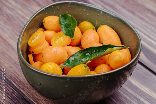 side view  of fresh ripe kumquats with water drops in a bowl on rustic wooden background