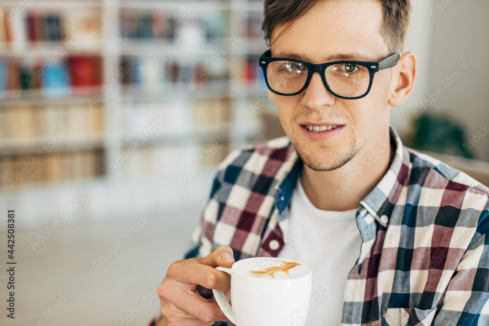 smiling young man drinking coffee from a mug, Handsome young man drinking coffee while sitting in a cafe