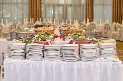 Wallpaper Mural Catering table with a white tablecloth and six stacks where there are a lot of white plates and prepared salads in a large banquet hall with windows Torontodigital.ca