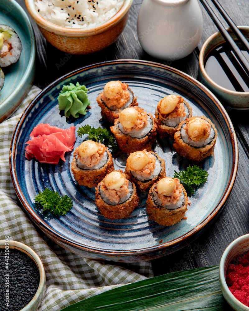 side view of baked sushi rolls with shrimps  ginger and wasabi on a plate served with soy sauce on wooden background