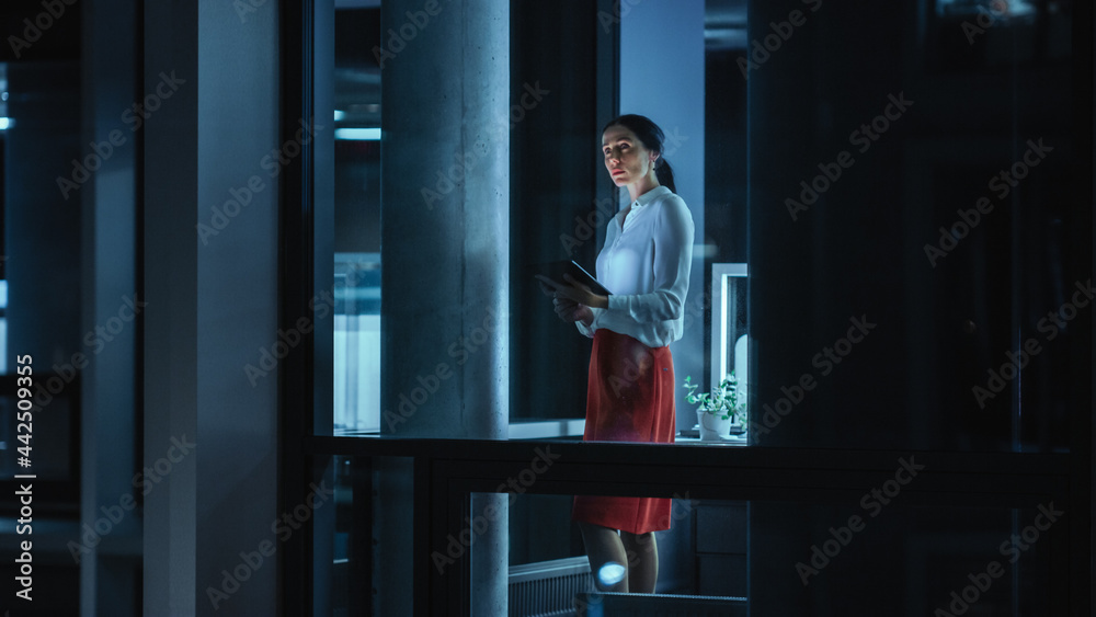 Fototapeta premium Shot from Outside: Businesswoman Working on a Tablet Computer in the Office. Manager Checking Emails while Standing by the Window. Employee Planning Financial Tasks and Business Development.