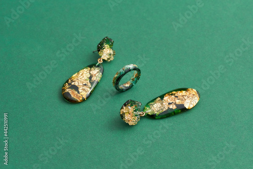 Set of a ring and dangle earrings made of epoxy resin with golden foil inside isolated over green background