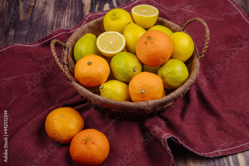 Fototapeta Naklejka Na Ścianę i Meble -  side view of fresh ripe lemons and oranges in a wicker basket on dark red fabric on rustic background