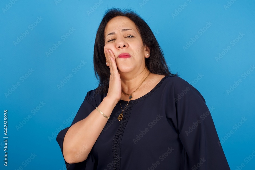 middle aged Arab woman standing against blue background with toothache middle aged Arab woman standing against blue background with toothache
