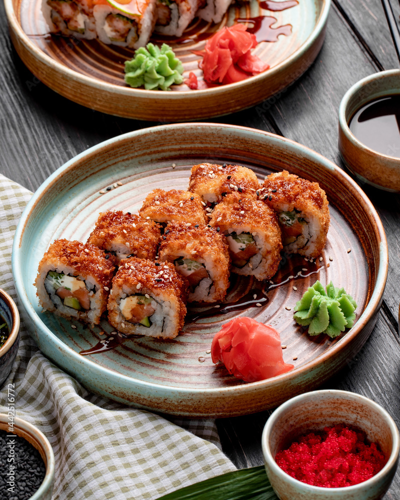 side view of hot fried sushi rolls with salmon avocado and cheese served with ginger and wasabi on a plate on wooden background