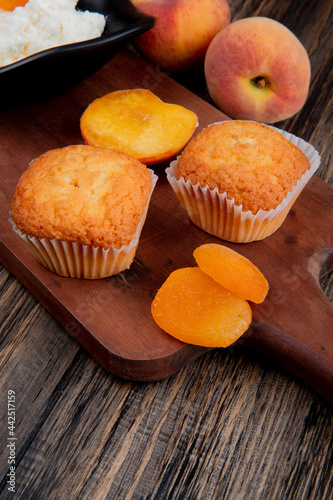 side view of muffins with dried apricots on wooden cutting board and fresh peaches on rustic background