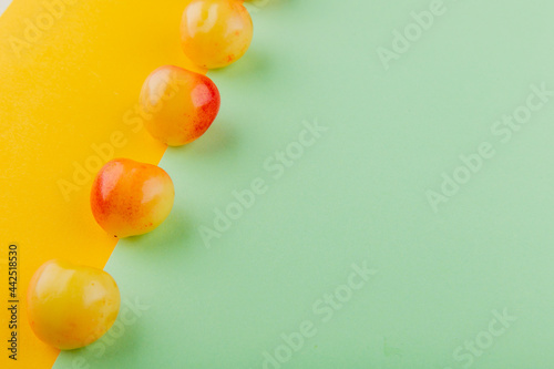 side view of ripe rainier cherries lined in a row on yellow and mint color background with copy space © HN Works