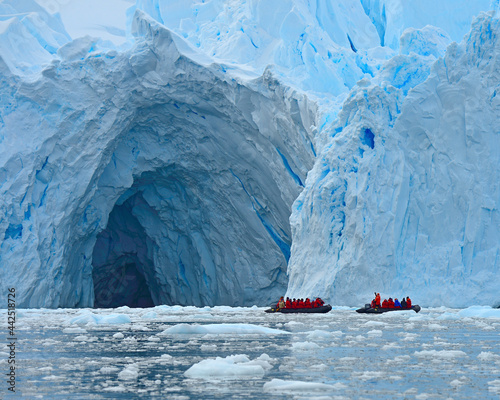 Two zodiac vessels explore the entrance of a large ice cave at the edge of an enormous glacier - Antarctica  photo