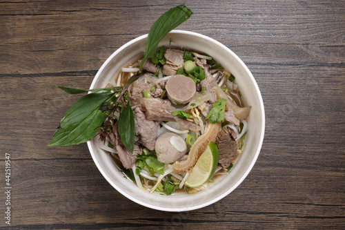 Vietnamese poh beef noodles soup broth with beef ball brisket tripe stomach parts been sprout thai basil lime in bowl on wooden table photo