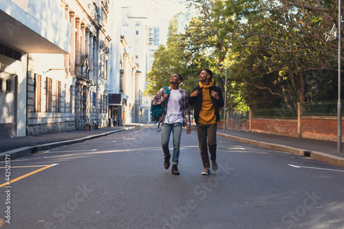 Wallpaper Mural Two happy mixed race male friends carrying backpacks walking in city street Torontodigital.ca