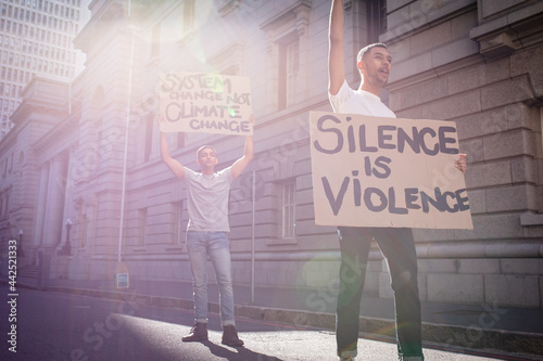 Two mixed race male friends carrying protest signs with slogans in sunny city street photo