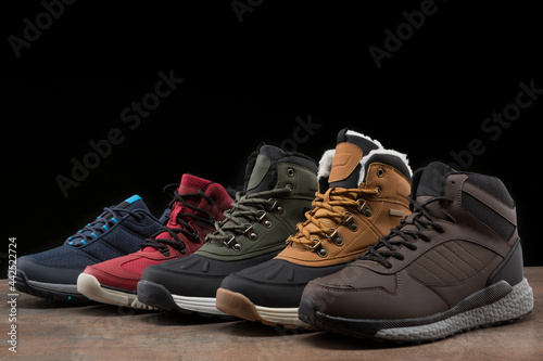 five winter boots of different colors, stand in a row, one after the other, on a black background, concept