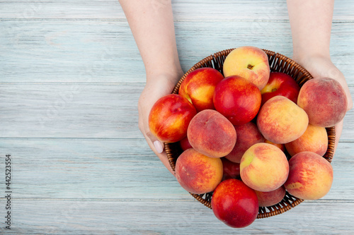 Cuadro en lienzo top view of female hands holding a wicker basket with fresh ripe nectarines and