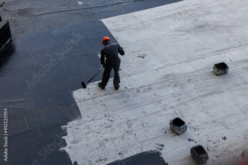 Waterproofing coating. A worker applies bitumen mastic to the foundation. Roofer cover the waterproofing primer on the roof, modified with polymer bitumen, with a roller brush. photo
