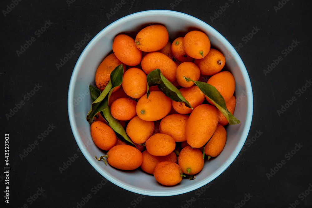 top view of fresh ripe kumquats in a blue bowl on black background
