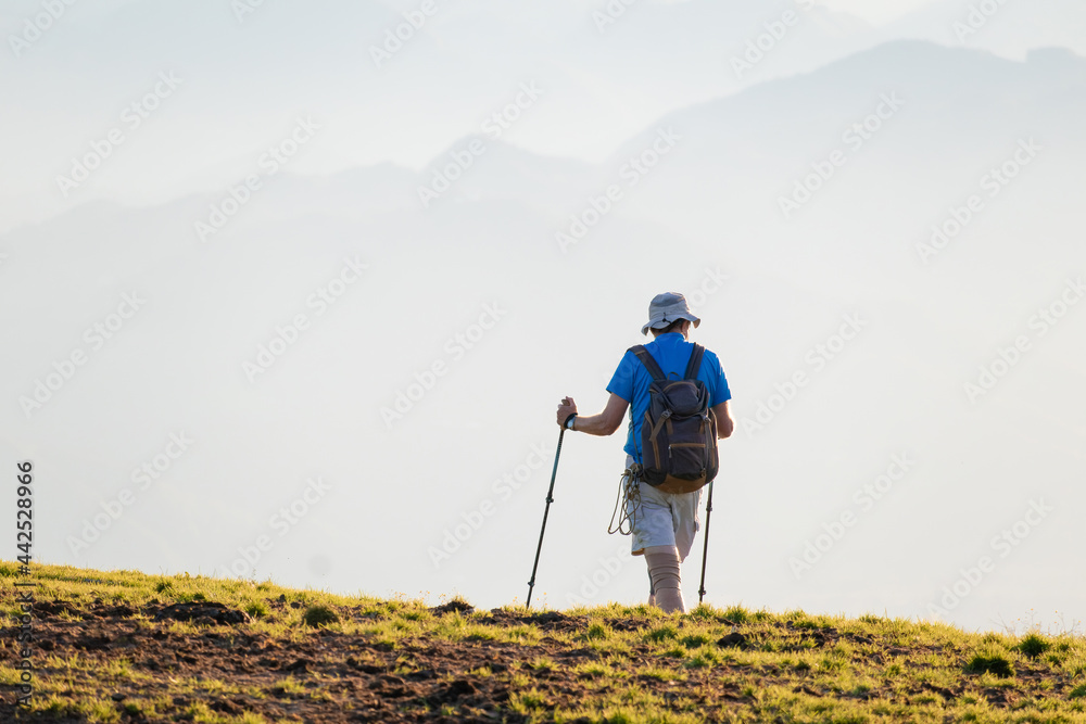 Hiker with backpack and walking sticks on a mountain at sunset.