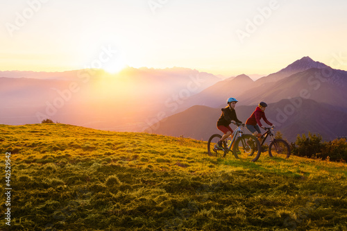Mother and daughter cycling on mountain bikes at a sunset in mountains. © 24K-Production
