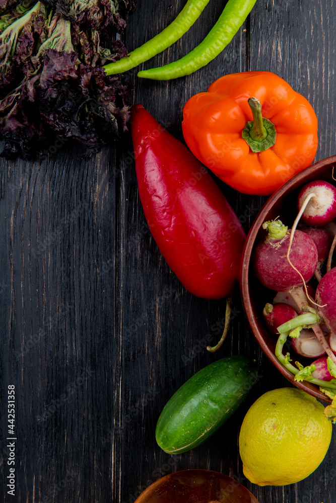top view of fresh vegetables colorful bell peppers green chili pepper lettuce and radish in a bowl on dark wooden background
