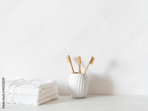 Minimal bath background with bamboo toothbrushs in ceramic glass and swhite towels