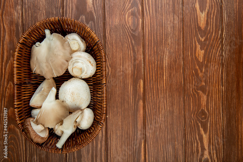 top view of fresh white mushrooms in a wicker basket on rustic wooden background with copy space