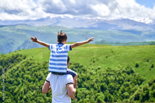 the child rides on the shoulders of his father with his arms spread out. summer of the mountain. fresh air. rest