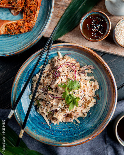 top view of salad with chopped cabbage chicken and black seeds in a plate with chopsticks on wooden background