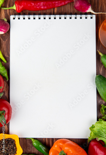 top view of sketchbook and fresh vegetables colorful bell peppers green chili peppers tomatoes and black peppercorns on rustic wooden background