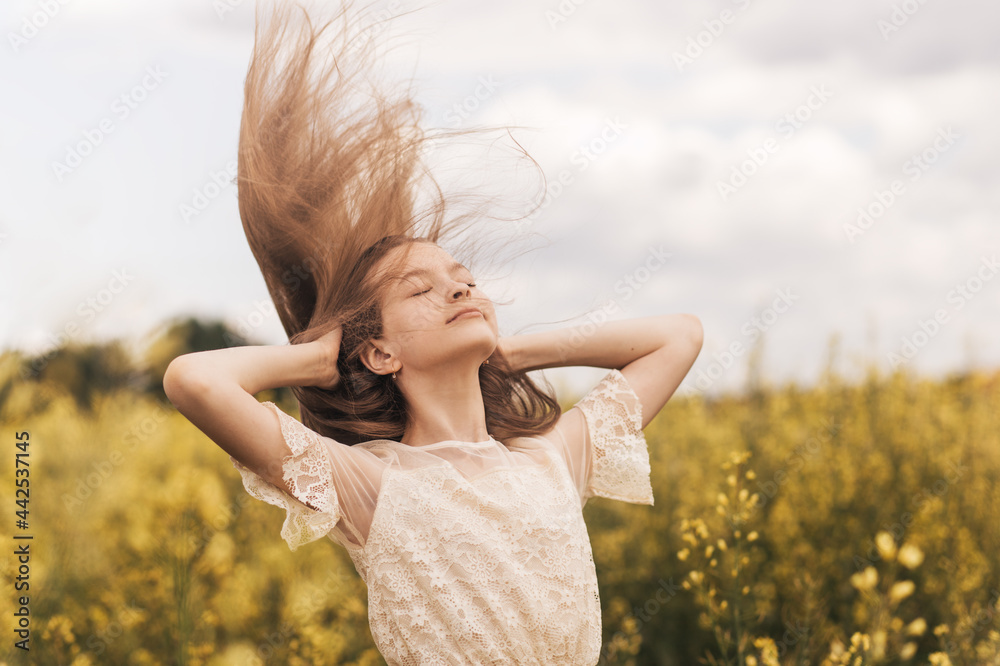 Young beautiful girl with long hair flying in the wind against the background of rapeseed field. Breeze playing with girl's hair Young beautiful girl with long hair flying in the wind against the background of rapeseed field. Breeze playing with girl's hair