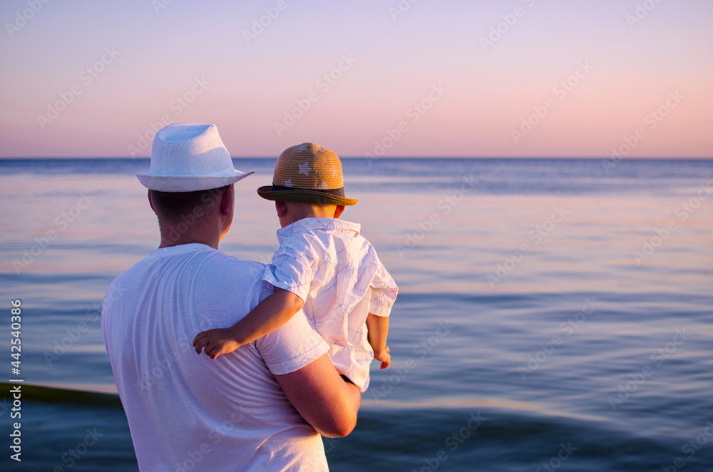 Dad and son look at the sea sunset
