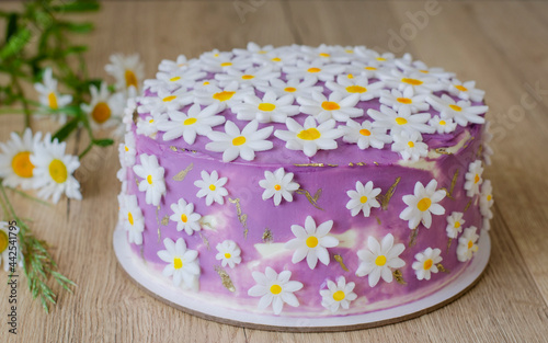 Purple cake with a decor of white daisies on a wooden background