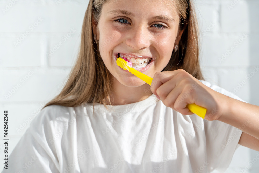 Beautiful little girl child brushing her teeth against the background of a white brick wall in a sunny bathroom. The concept of hygiene and oral care Beautiful little girl child brushing her teeth against the background of a white brick wall in a sunny bathroom. The concept of hygiene and oral care
