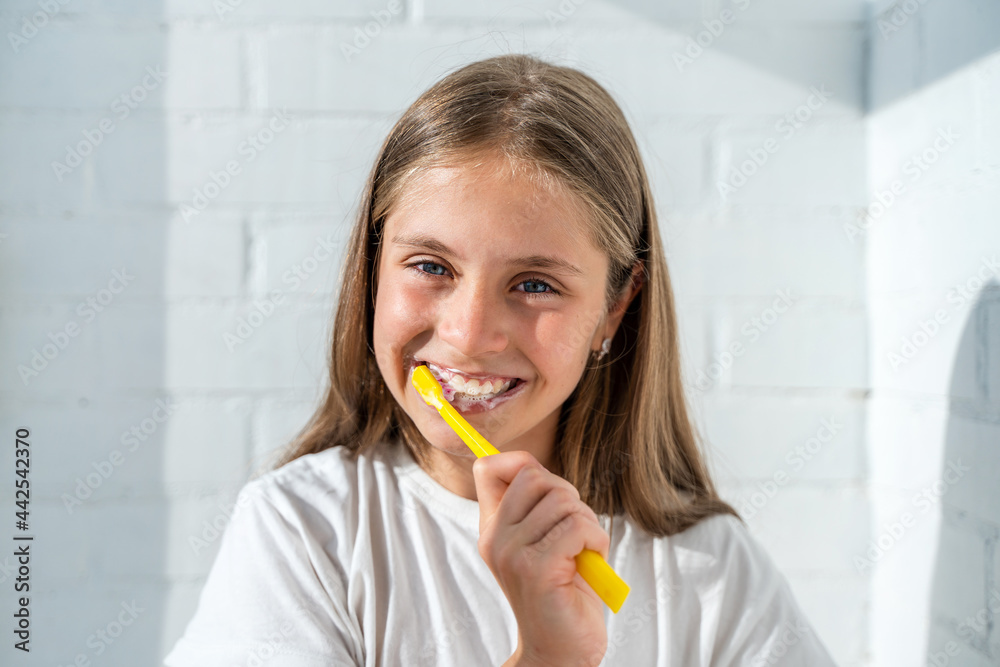 Beautiful little girl child brushing her teeth against the background of a white brick wall in a sunny bathroom. The concept of hygiene and oral care Beautiful little girl child brushing her teeth against the background of a white brick wall in a sunny bathroom. The concept of hygiene and oral care