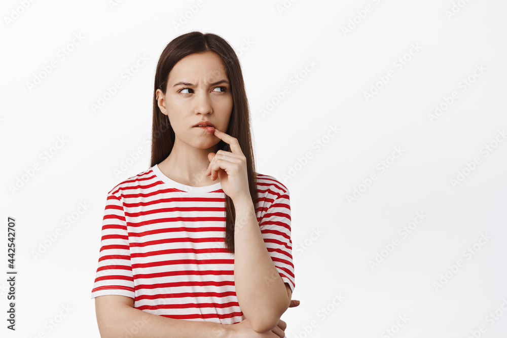 Image of thoughtful girl furrow eyebrows and bite lip ponder, thinking of smth, looking aside and squinting suspicious, standing against white background Image of thoughtful girl furrow eyebrows and bite lip ponder, thinking of smth, looking aside and squinting suspicious, standing against white background