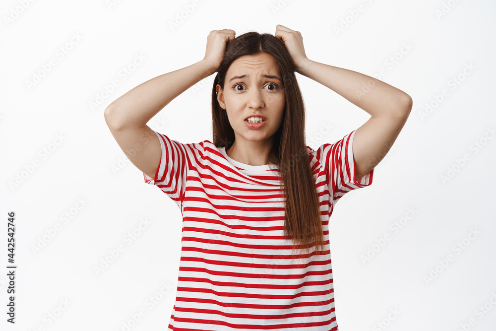 Girl in trouble holds hands on head, panicking. Alarmed young woman looking anxious and worried, distressed and frustrated with big problem, standing against white background Girl in trouble holds hands on head, panicking. Alarmed young woman looking anxious and worried, distressed and frustrated with big problem, standing against white background